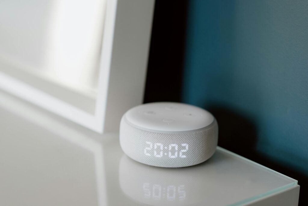 Close-up of a smart speaker with an illuminated 20:02 LED clock display on a desk.